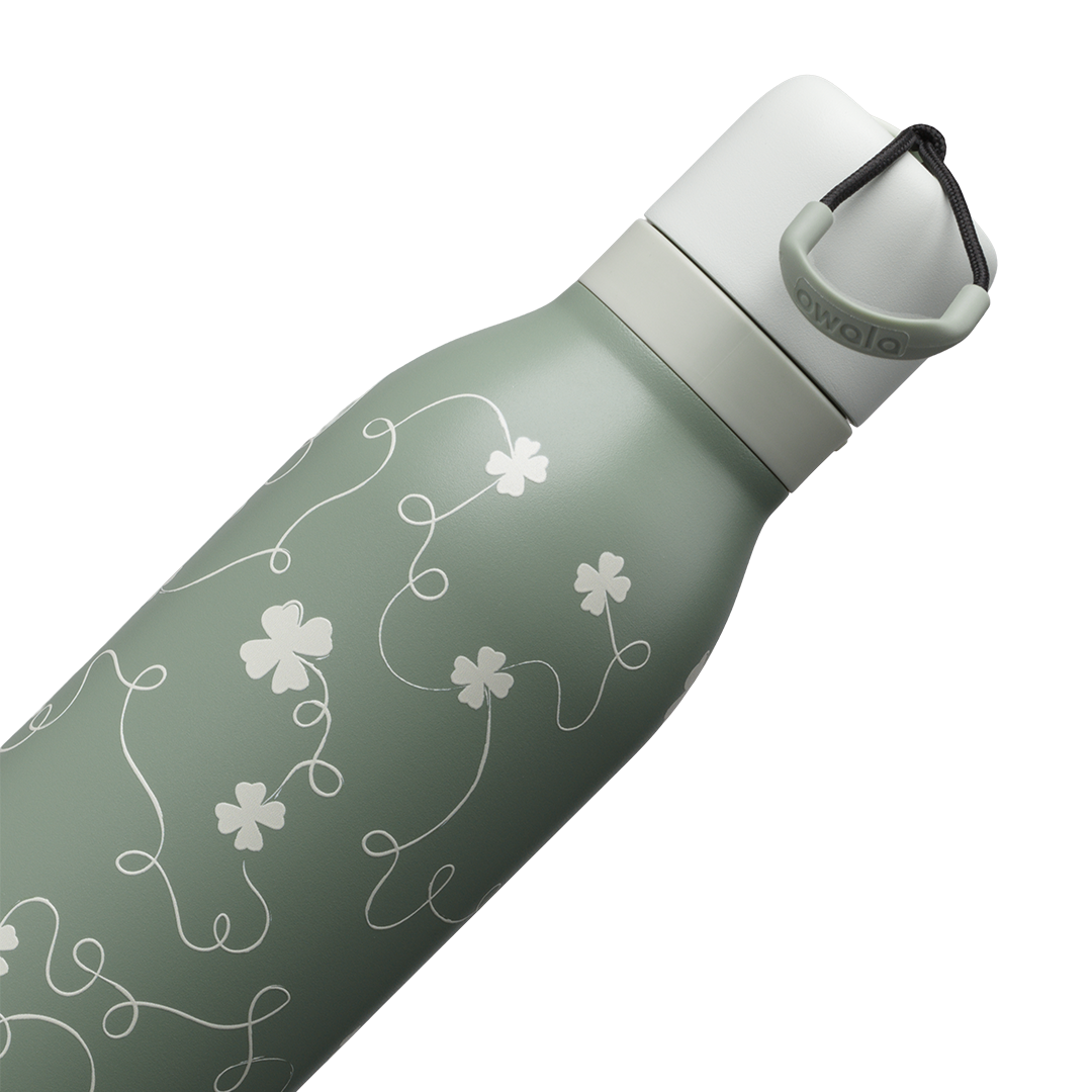 Owala FreeSip Twist 24oz in Clover Achiever, close-up of the sage green body with white clover and vine pattern and the white twist cap with sage carry string and dark carry string grip